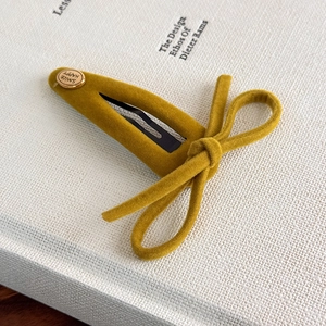 Macro view of ginger yellow velvet bow hair clip with engraved smile happy gold metal stud