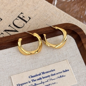 Macro detail of gold irregular twisted geometric C-shaped earrings on a wooden display