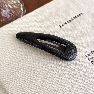 Detail of a vintage black snakeskin textured teardrop hair clip on a minimalist background