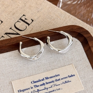 Macro detail of silver irregular C-shaped earrings with molten texture and metallic finish
