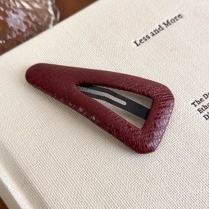 Close-up of vintage burgundy leather textured hair clip on a minimalist book background