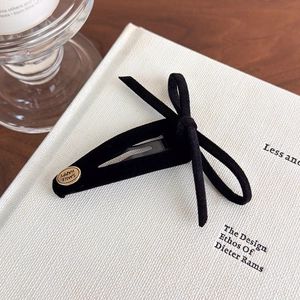 Close-up of black velvet bow hair clip with gold logo on a minimalist background
