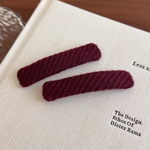 Close-up of deep burgundy knitted fabric hair clip on a textured white book surface