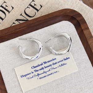 Detailed view of silver twisted C-shaped earrings on a linen jewelry display tray