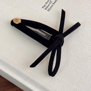 Close-up of black velvet bow hair clip with gold smile happy engraved metal button