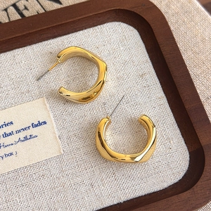 Detail of chunky gold twisted C-shaped hoop earrings with a polished geometric finish