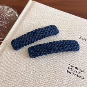 Close-up of navy blue knitted BB hair clips with fine twill texture on a book