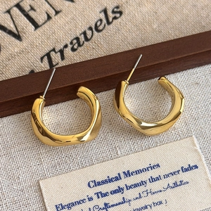 Close-up of golden wavy hoop earrings featuring a vintage textured C-shape design
