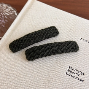 Detailed macro view of dark green knitted rectangular hair clips on a white book surface