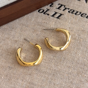 Detailed macro view of gold irregular C-shape hoop earrings on a textured linen background