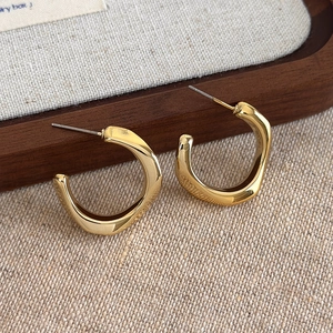 Detailed macro view of irregular gold twisted square hoop earrings on a wooden tray