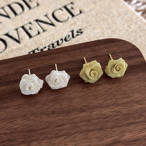 Detail shot of mesh rose earrings in gold and silver finish on a rustic wooden background