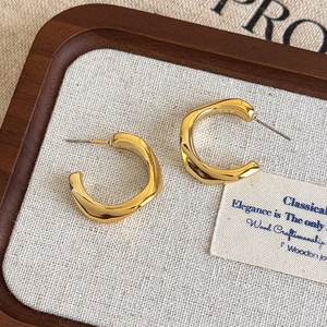 Detail shot of golden C-shaped hoop earrings with wavy texture in a wooden jewelry box
