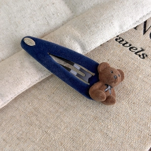 Détail macro d'une pince à cheveux en velours bleu marine avec un petit ours en peluche
