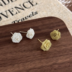 Detail of woven wire rose earrings in gold and silver finish on a wooden display