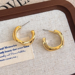 Detailed macro view of irregular golden C-shaped hoop earrings with wavy design in a tray