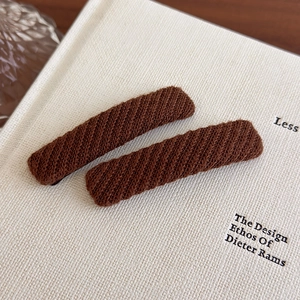 Detail of dark brown knitted rectangle hair clips on a white book and wooden table
