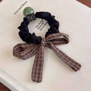Détail d'un chouchou à carreaux avec nœud, perle verte et étiquette Hand Made