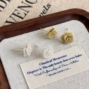 Detail of gold and silver mesh rose stud earrings with woven texture on linen