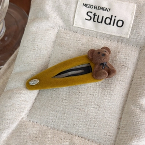 Détail d'une pince à cheveux vintage en velours jaune moutarde avec un ours floqué