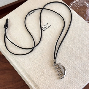 Vue rapprochée d'un collier pendentif peigne argenté sur un livre avec cordon noir minimaliste
