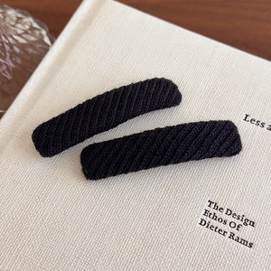 Close-up of minimalist black knitted rectangular hair clips on a textured book surface