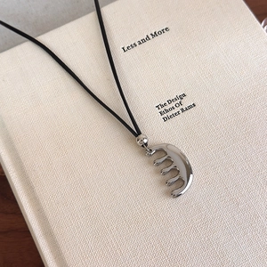 Détail d'un collier avec pendentif peigne argenté posé sur un livre texturé