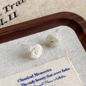 Macro shot of white copper mesh rose earrings with detailed wire texture on wood