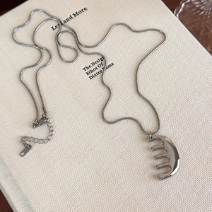 Collier argenté avec pendentif peigne sur livre blanc, bijou élégant et minimaliste