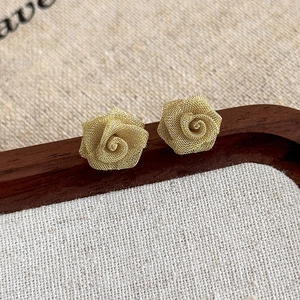 Detailed close-up of golden copper mesh rose earrings on a vintage wooden tray