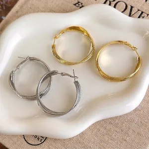 Matte gold and silver multi-layer twisted hoop earrings on white decorative tray