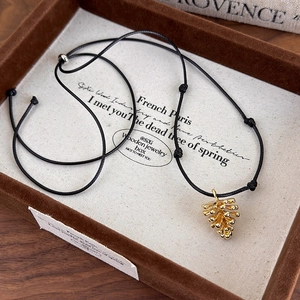 Detail of a golden pinecone pendant on an adjustable black cord necklace for sweaters