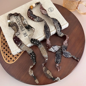 Détail du collier en tissu à motif paisley montrant la texture plissée et la perle décorative