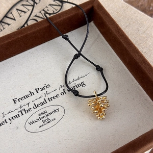 Macro detail of a golden pinecone pendant on adjustable black cord in a vintage jewelry box