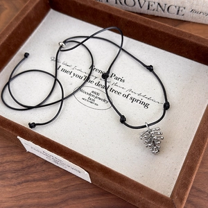 Detailed shot of silver pinecone pendant on adjustable black rope in a wooden box