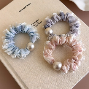 Three elegant scrunchies with lace trim and pearls displayed on an open book cover