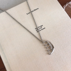 Vue macro d'un collier pendentif peigne argenté poli sur une surface texturée crème