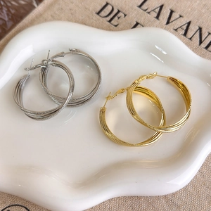 Close-up of twisted layered hoop earrings in gold and silver on a white ceramic tray