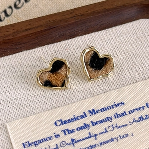 Gros plan de boucles d'oreilles cœur léopard avec bord doré sur une toile de lin rustique