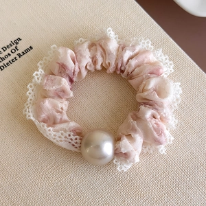 Close-up of pink textured scrunchie featuring white lace edges and a glossy pearl detail
