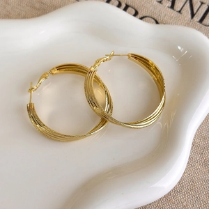 Detail of layered gold hoop earrings with matte and polished finish on white tray