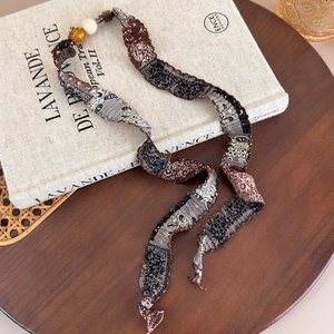 Détail du collier en tissu cachemire avec perles en bois et texture plissée sur un livre