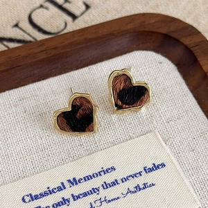 Détail de boucles d'oreilles cœur à imprimé léopard avec bordure dorée sur un tissu en lin