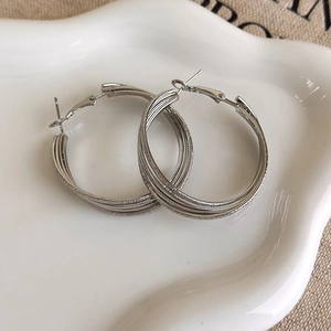 Detail shot of silver multi-layered hoop earrings with a matte texture on a ceramic plate