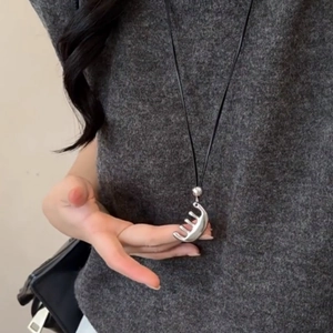 Collier minimaliste avec pendentif peigne argenté et cordon noir sur pull gris