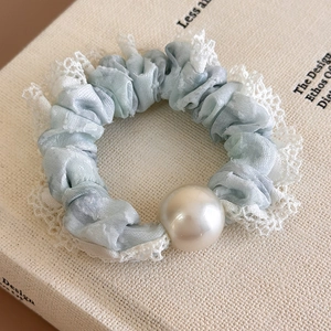 Macro detail of blue scrunchie with lace trim and large pearl bead on a book page