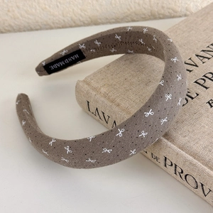 Close-up of taupe fabric headband featuring white bow print and HAND MADE label