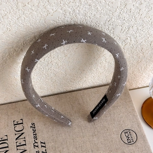 Close-up of handmade brown sponge headband with white embroidered bow and interior tag