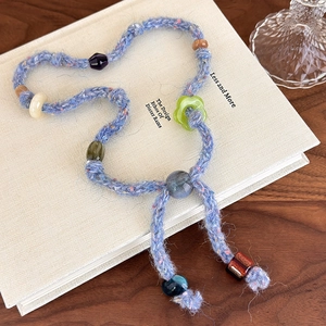 Detailed close-up of handmade blue knit sweater chain necklace with colorful beads on book