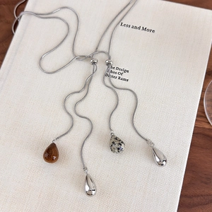 Detailed view of silver snake chain necklace with multi-material teardrop stone pendants